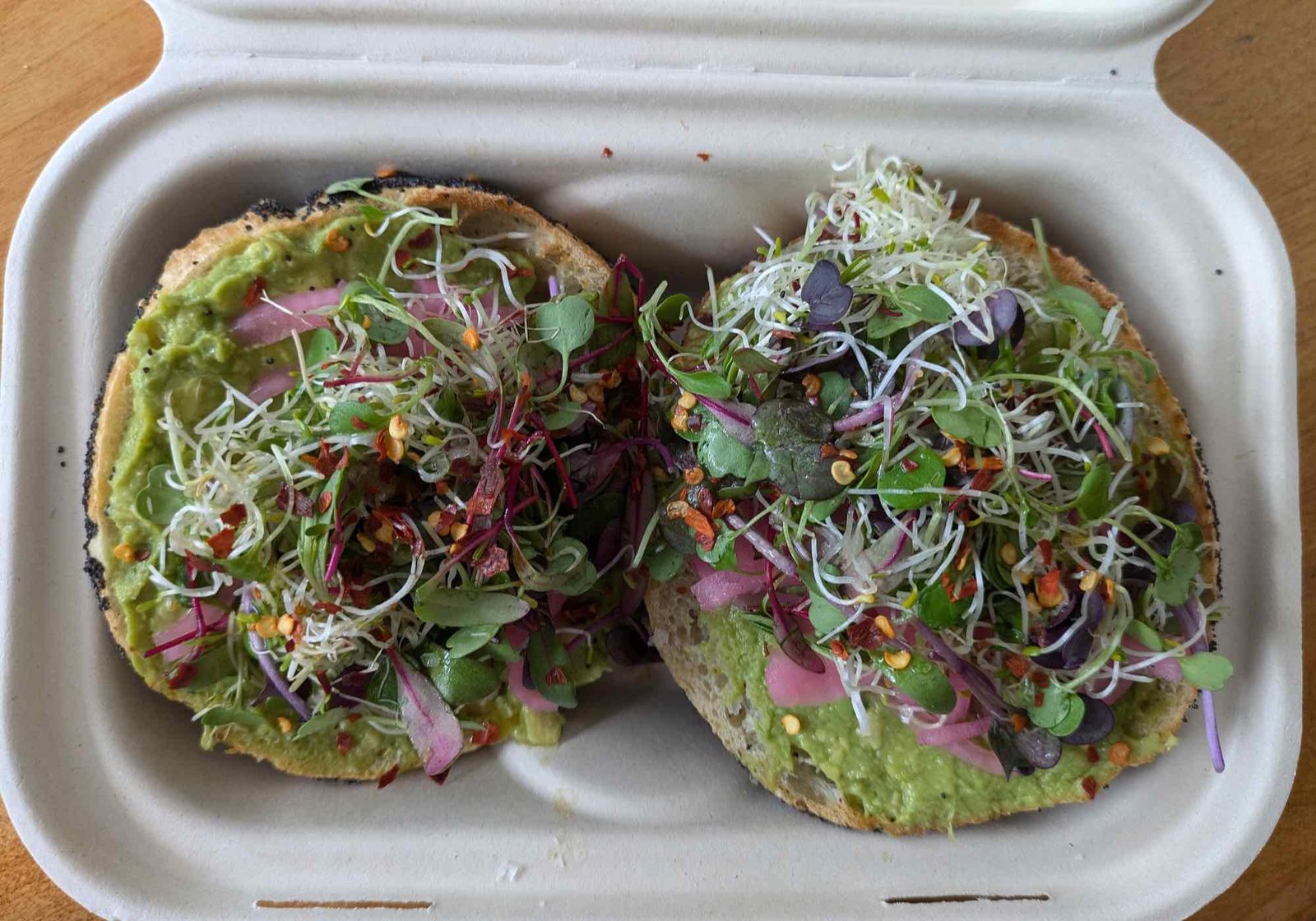 Aufgeschnittener Bagel mit Avocadocreme und Sprossen in einer Box